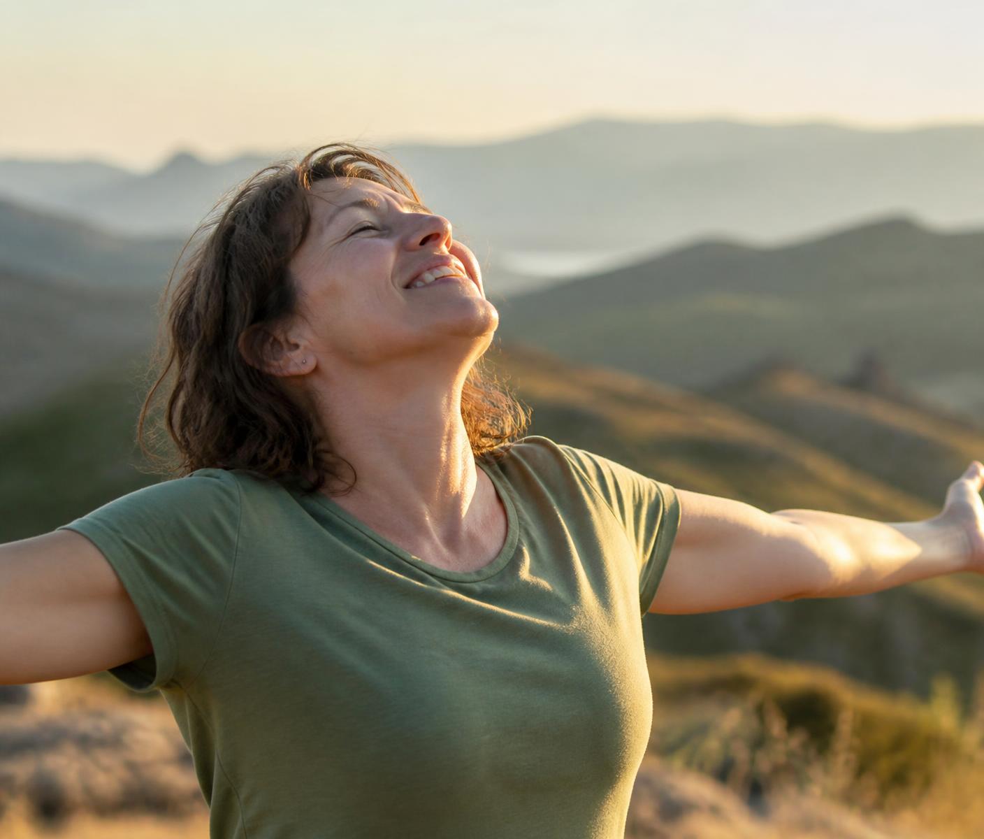 Woman standing outdoors at sunset with her arms open, feeling well again